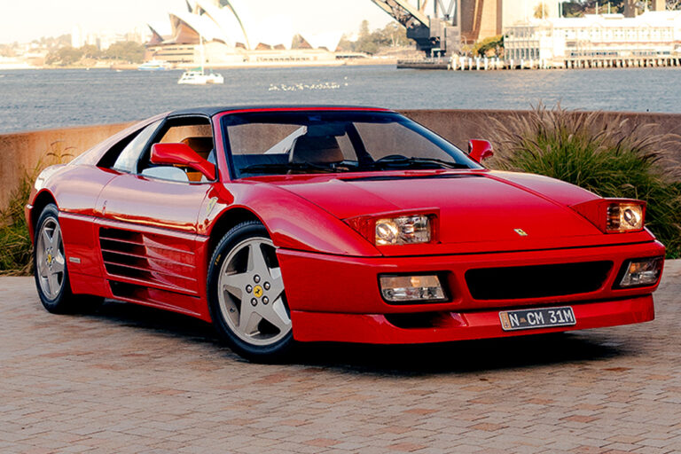 Red 1991 Ferrari 348 TS with pop-up headlights raised, parked on a harbourside promenade