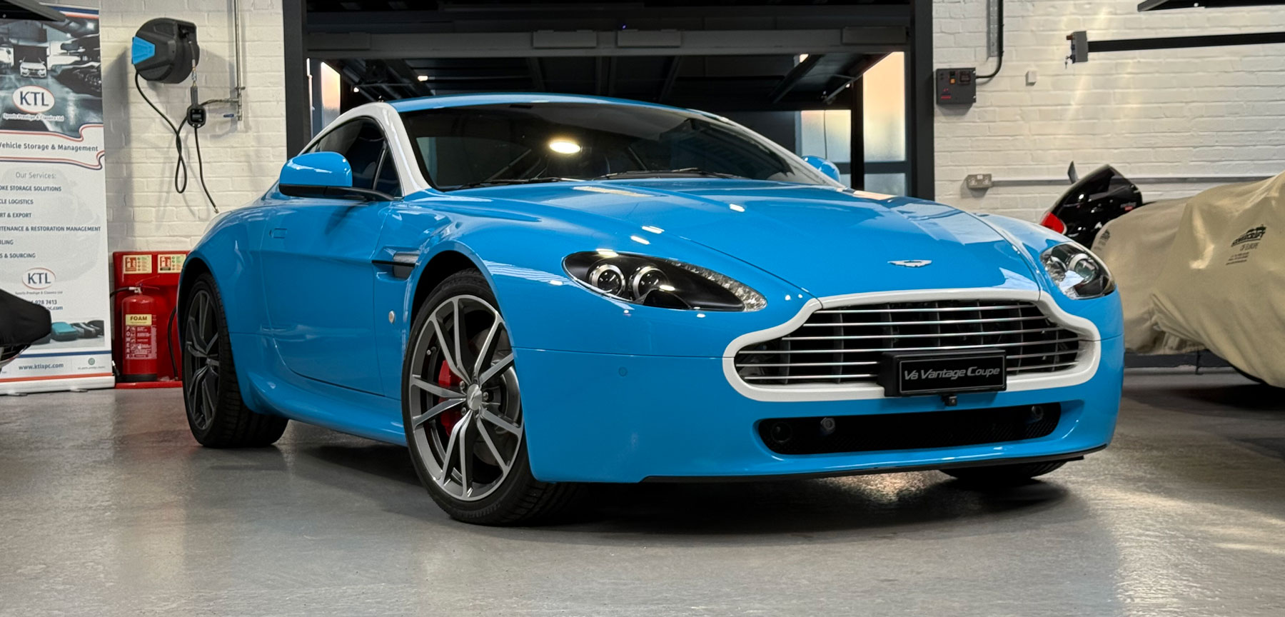Blue 2010 Aston Martin V8 Vantage front three-quarter view in a classic car storage garage