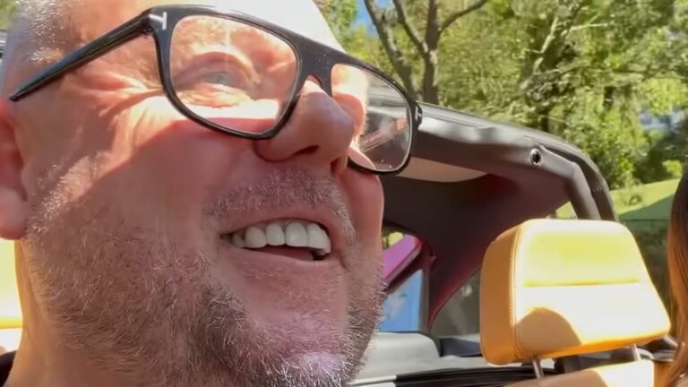 Tony Hilton smiling while driving an open-top classic car